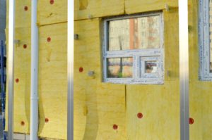 Exposed, yellow insulation on a wall with square windows and metal support beams